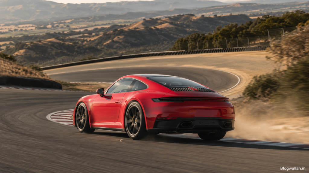 Red Porsche 911-style sports car driving through a Laguna Seca-style corkscrew corner on a California race track.